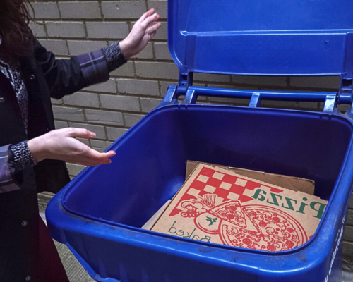 A pizza box in a recycling bin with a woman closing the lid